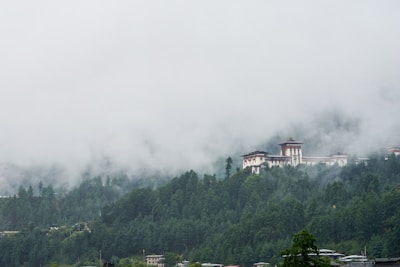 white and brown concrete building surrounded by green trees under white clouds during daytime