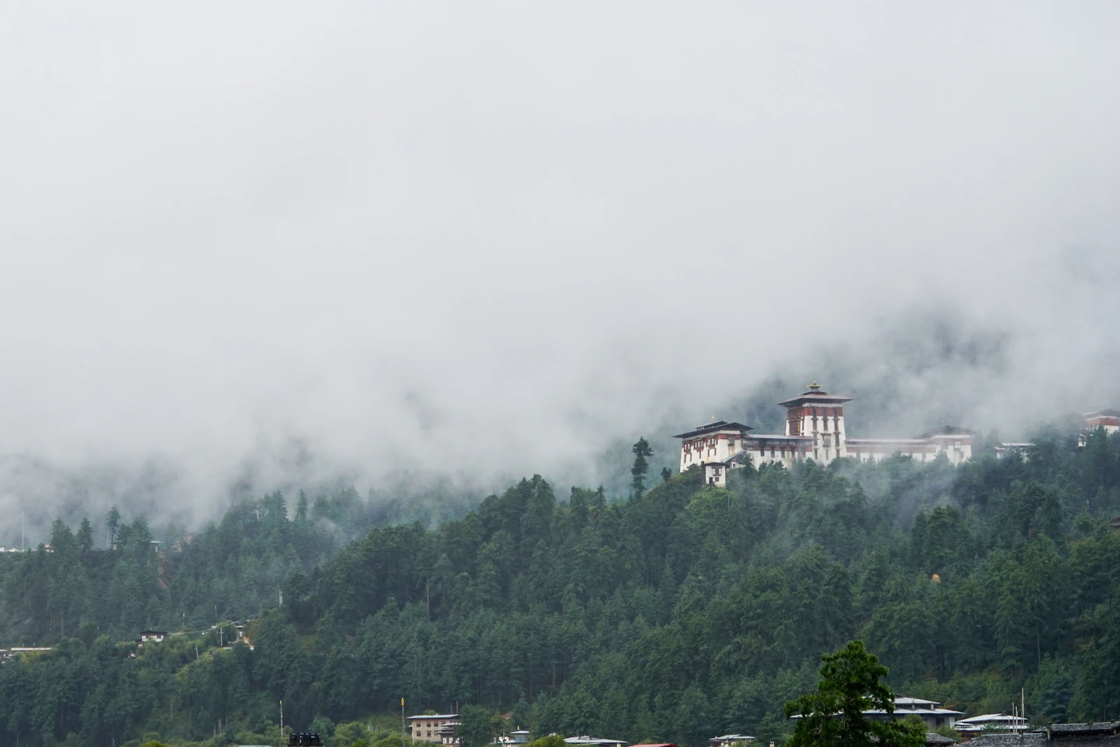 Jakar Dzong on its ridge above the Bumthang valley, low cloud drifting over the forest below
