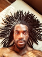 A person with long, spread-out dreadlocks lies on a light-colored surface. The lighting casts soft shadows and highlights the texture of the hair.