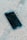 A smartphone with a cracked screen lies on a rough concrete surface. The cracks spread across most of the display, indicating significant damage.