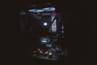 A dimly lit computer interior showcasing components such as cooling fans, RAM sticks, and a lit 'Cooler Master' logo. The setup includes various cables and an illuminated interior lighting system with a dark, moody atmosphere.