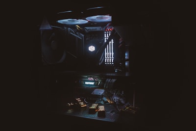 A dimly lit computer interior showcasing components such as cooling fans, RAM sticks, and a lit 'Cooler Master' logo. The setup includes various cables and an illuminated interior lighting system with a dark, moody atmosphere.