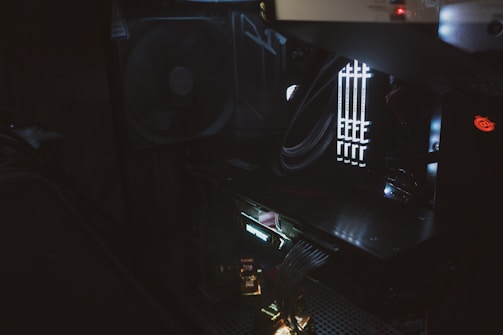 The image captures the interior of a computer case, highlighted by faint lighting. Visible components include cooling fans, multiple memory sticks, and various cables neatly organized. The lighting emphasizes the sleek and organized build of the computer hardware.