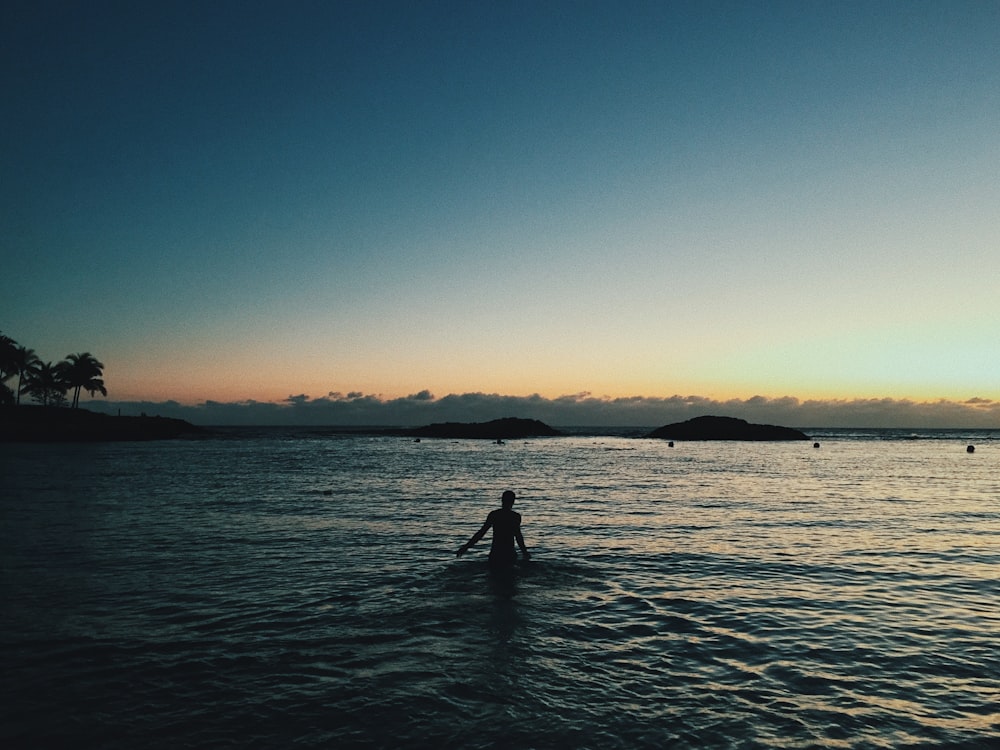 silhouette of person standing on sea water during sunset