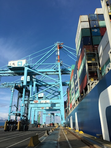 A panoramic view of a bustling industrial port with cargo ships being loaded with metal ores under a clear blue sky.