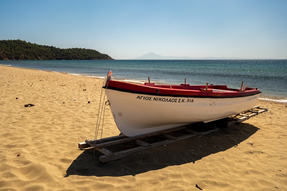 Barca rossa e bianca su sabbia marrone vicino allo specchio d'acqua durante il giorno