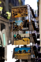 A display rack holds several colorful postcards, showcasing various scenes. The top postcard features a city skyline with historic architecture. Below it, a card displays a beach scene with people relaxing on the sand. The lower postcards also represent beachside and urban views, conveying a tourist-friendly vibe.