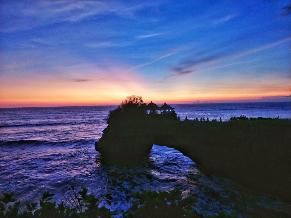 silhouette of rock formation on sea during sunset