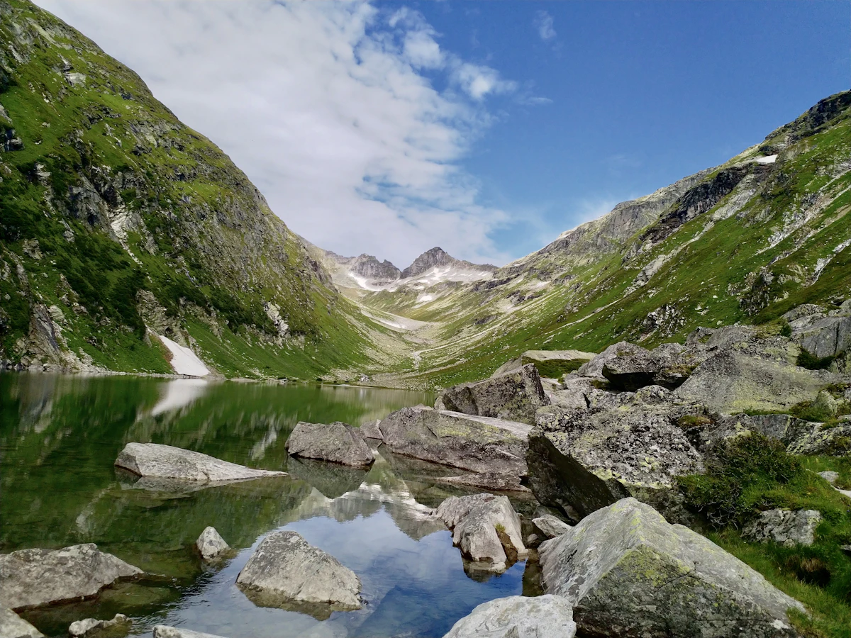 The Dorfersee above Kals am Großglockner, a still mountain lake with boulders on its shore and peaks at the head of the valley