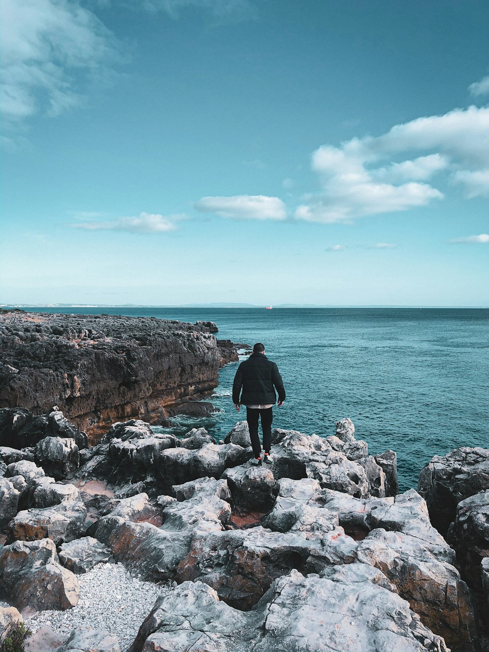 man in black jacket standing on rocky shore during daytime