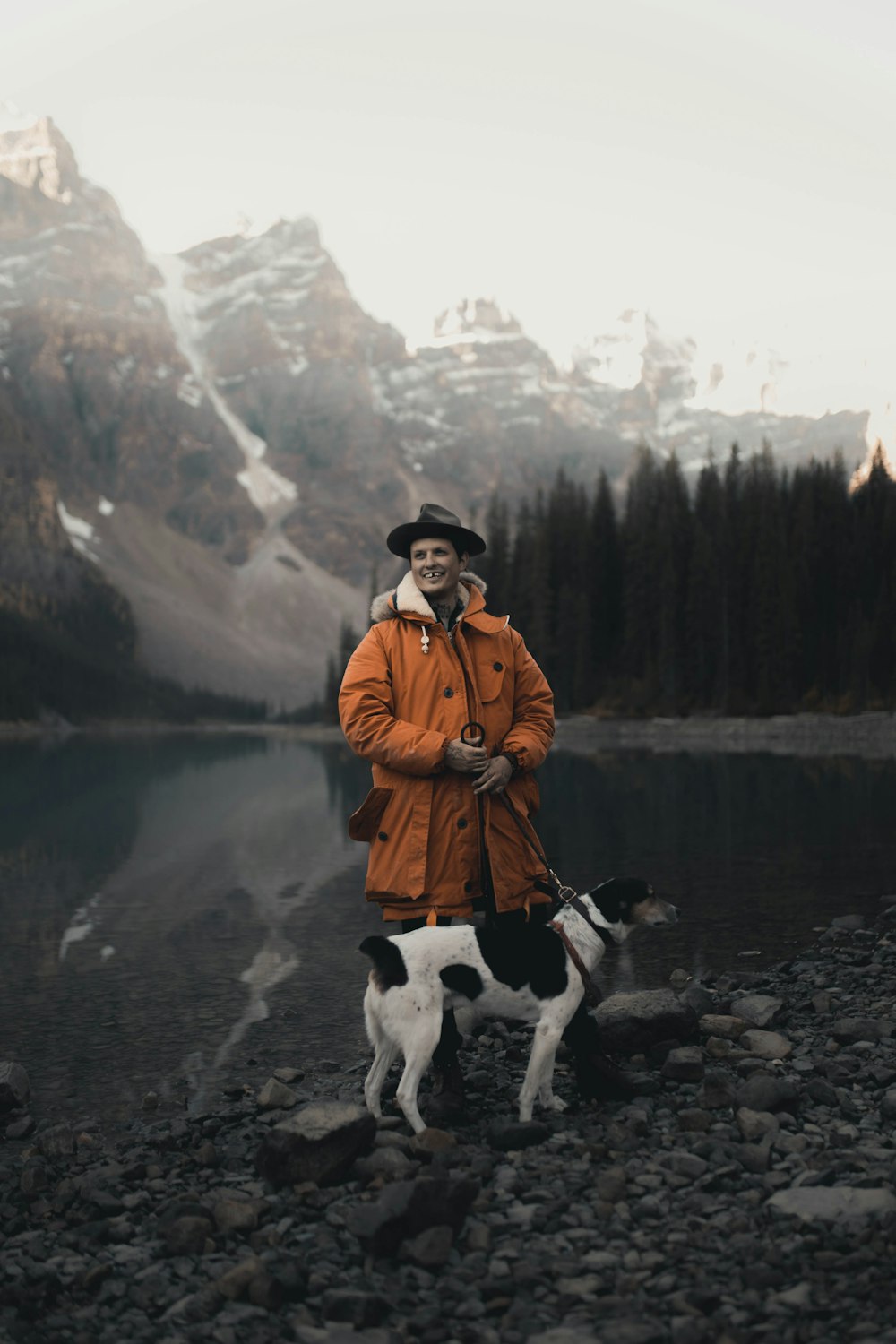 homme en veste marron debout à côté d’un chien près du lac pendant la journée