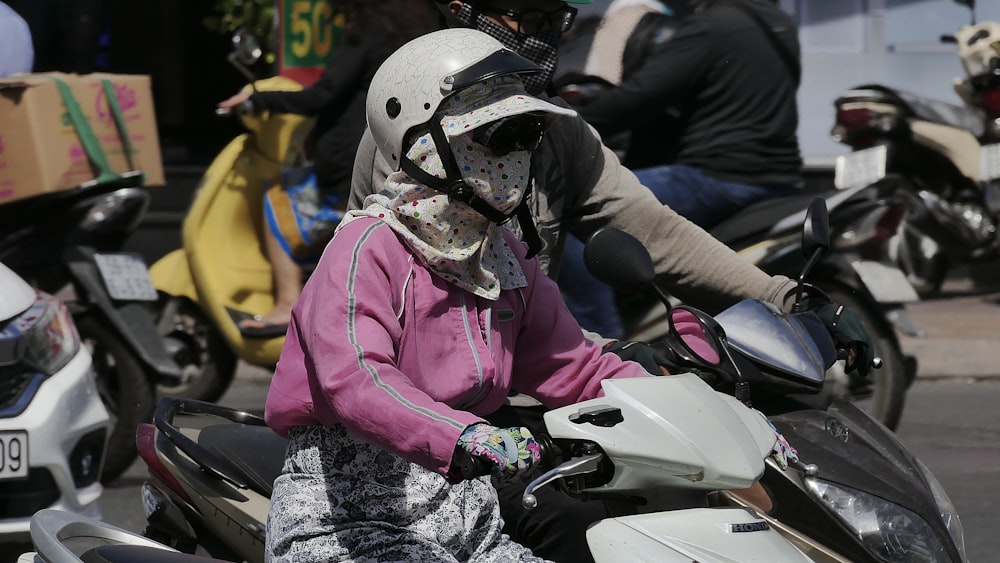 pessoa em jaqueta rosa vestindo capacete branco andando de moto branca e preta durante o dia