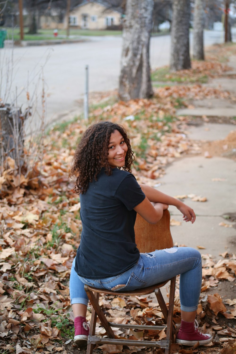 woman in black t-shirt and blue denim jeans sitting on brown dried leaves during daytime