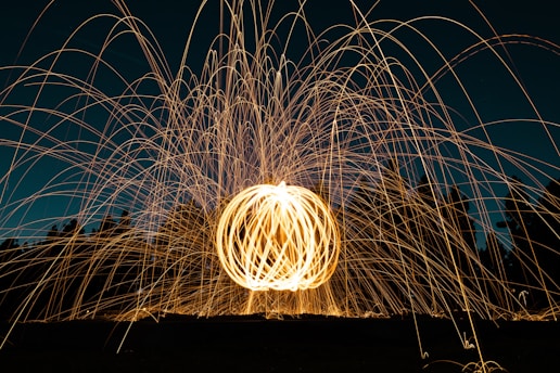 A vibrant display of light trails creating a spherical pattern, with bright, swirling lines against a dark background. The scene appears dynamic and lively, with the light arcs suggesting motion and energy.