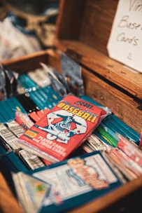 A collection of vintage baseball card packs is arranged inside an open wooden box. The cards are colorful, with a focus on a red pack featuring an illustration of a baseball player. A sign in the background reads 'Vintage Baseball Cards'.