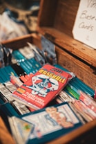 A collection of vintage baseball card packs is arranged inside an open wooden box. The cards are colorful, with a focus on a red pack featuring an illustration of a baseball player. A sign in the background reads 'Vintage Baseball Cards'.