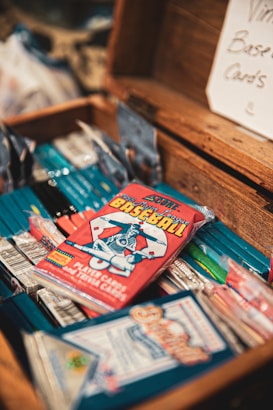 A collection of vintage baseball card packs is arranged inside an open wooden box. The cards are colorful, with a focus on a red pack featuring an illustration of a baseball player. A sign in the background reads 'Vintage Baseball Cards'.