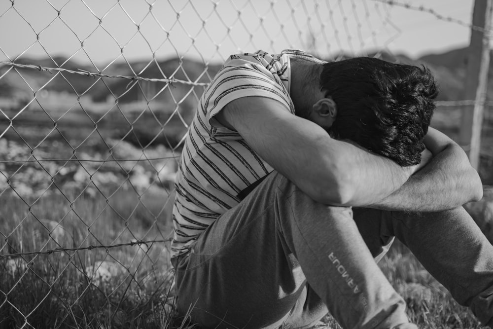 uomo in t-shirt a righe bianche e nere che si appoggia alla recinzione a maglie di catena