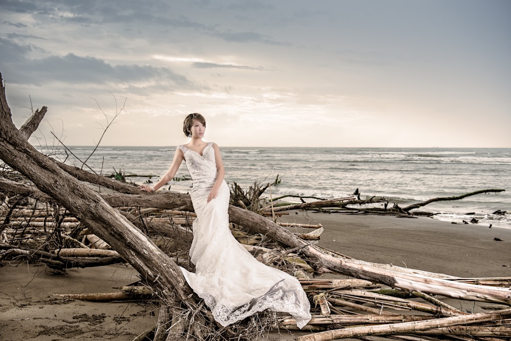 woman in white wedding dress standing on brown wood log near body of water during daytime
