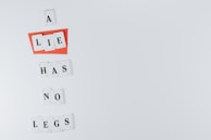 Text tiles arranged vertically spell out the phrase 'A LIE HAS NO LEGS' on a white surface, with the word 'LIE' emphasized by a red background underneath.
