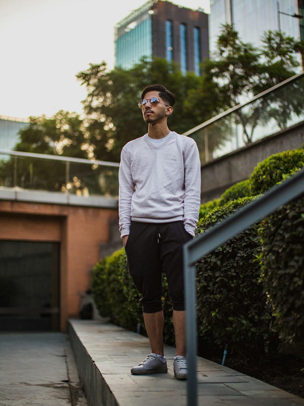 man in white crew neck long sleeve shirt and black shorts standing on gray concrete stairs