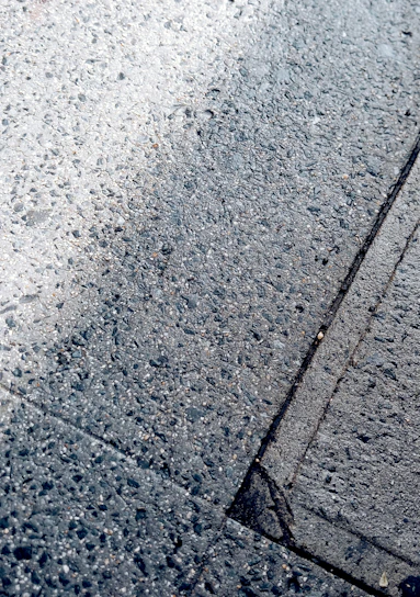 Close-up of freshly laid asphalt with smooth, dark texture reflecting sunlight.