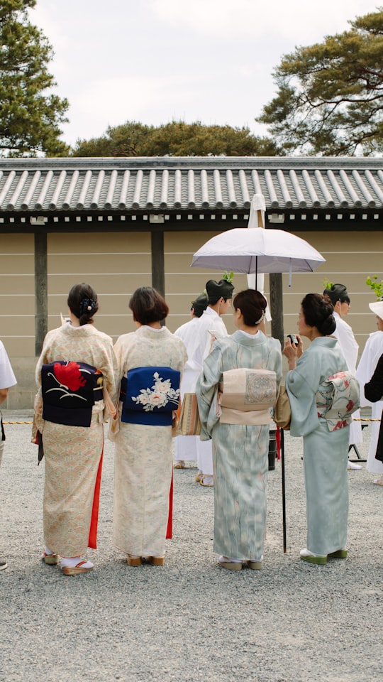 group of people wearing white and yellow floral kimono standing on gray concrete floor during daytime in 京都御苑 Japan