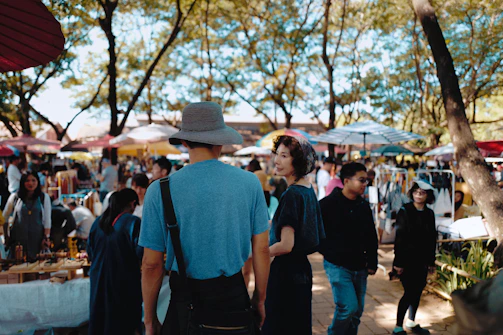 An outdoor cannabis market bustling with people, stalls, and vibrant green plants under a sunny sky.