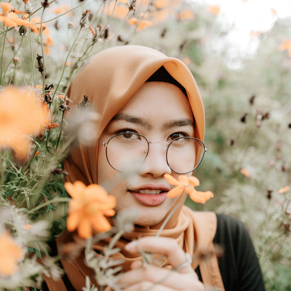 woman in brown hijab and black framed eyeglasses holding orange flowers