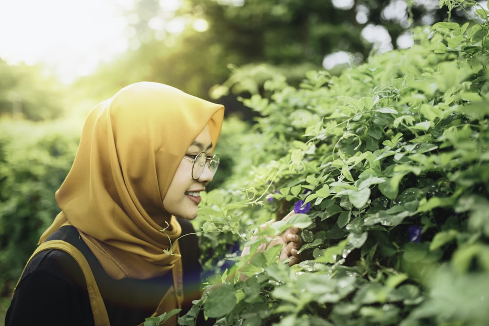 woman in yellow hijab and brown scarf standing beside green plant during daytime