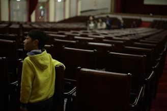 a young boy standing in a row of empty chairs