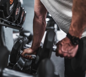 person in gray shirt holding black dumbbell