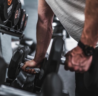 person in gray shirt holding black dumbbell