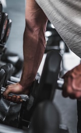 person in gray shirt holding black dumbbell