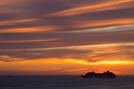 A luxurious cruise ship sailing at sunset with vibrant orange and pink skies.