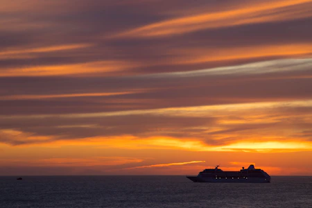 A vibrant sunset over turquoise Caribbean waters with a cruise ship in the distance.