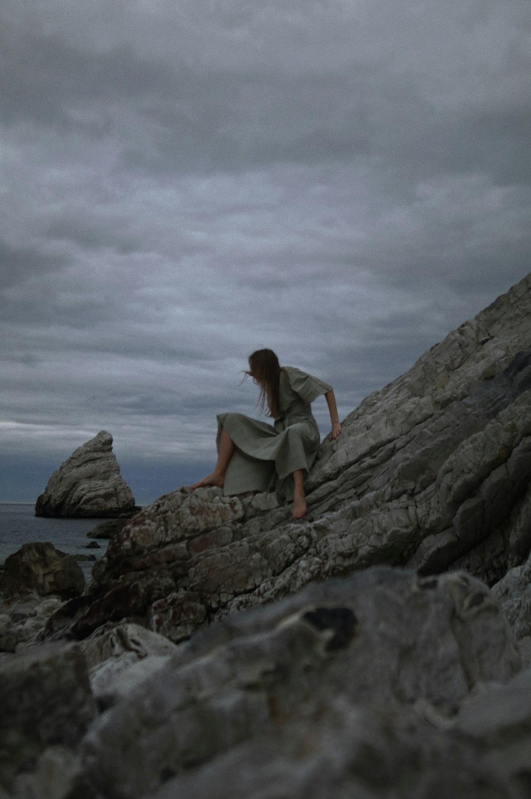 woman in white tank top sitting on rock formation near body of water during daytime