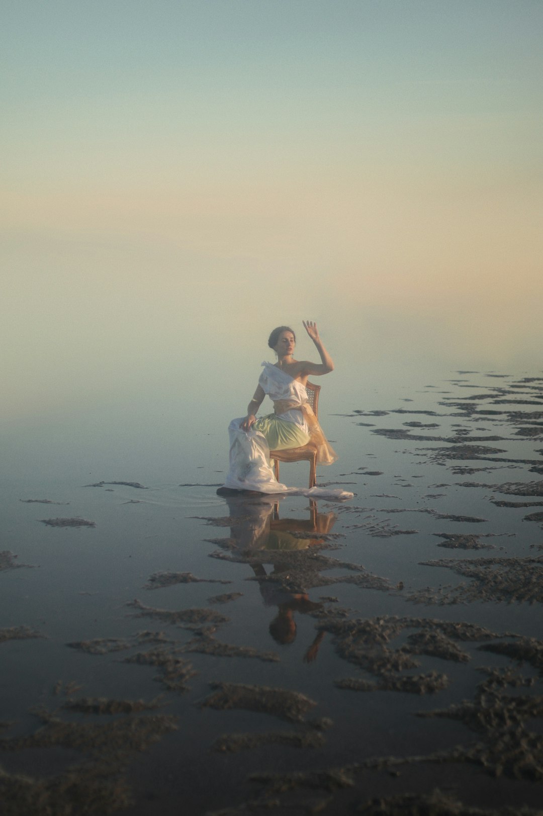 woman in white dress sitting on brown wooden chair on beach during sunset