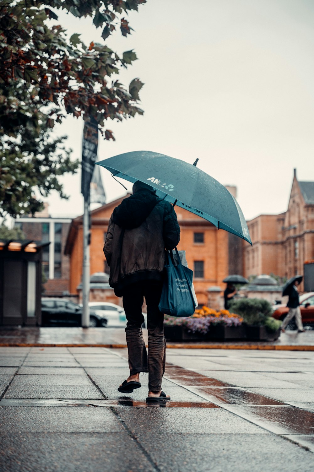 woman in black jacket and blue denim jeans holding umbrella walking on sidewalk during daytime