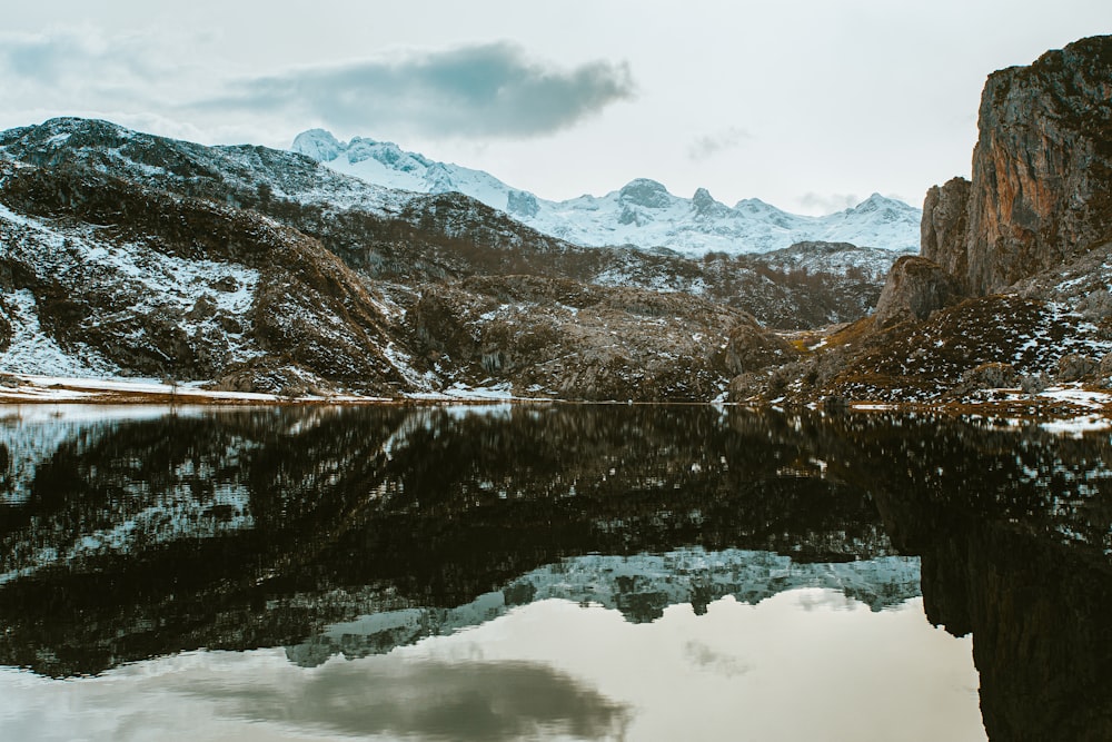 brown and green mountains beside lake under white clouds and blue sky during daytime