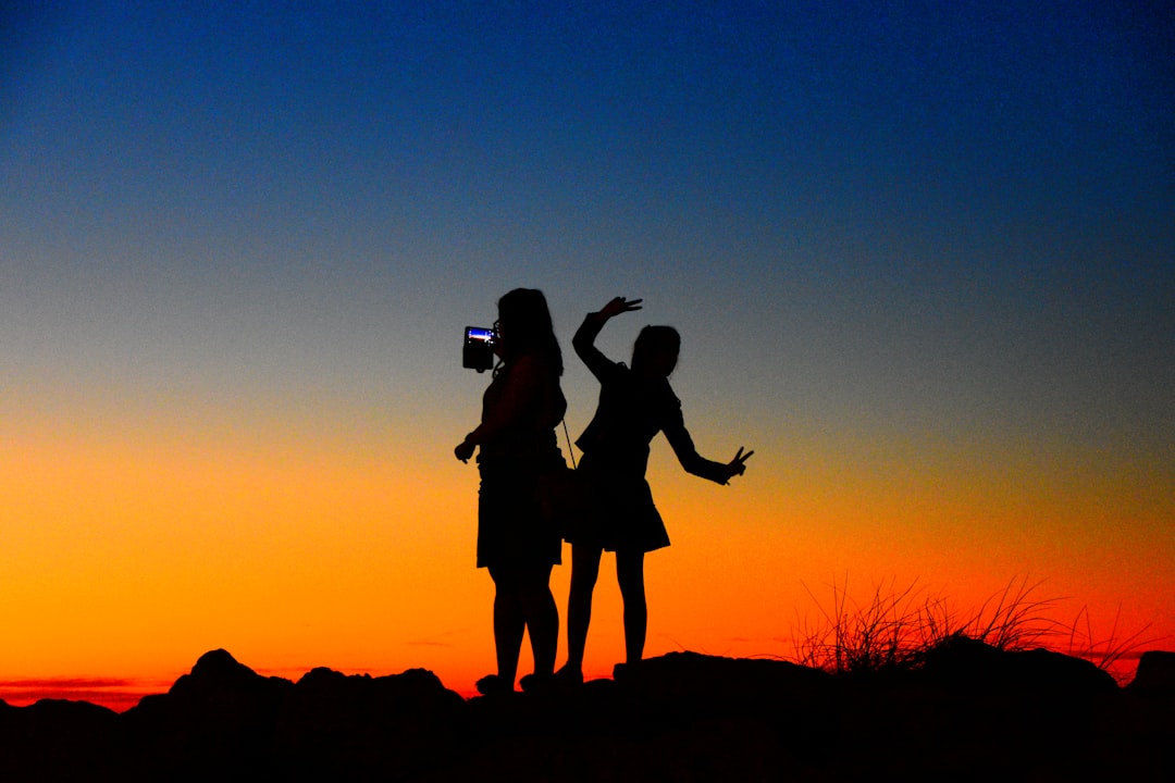 silhouette of 2 person standing on rock during sunset