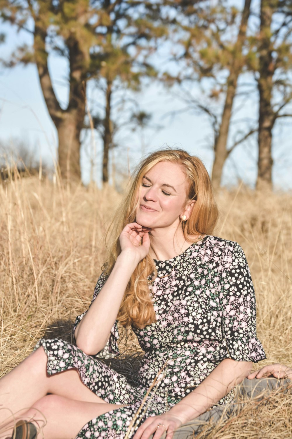 woman in black and white floral dress sitting on brown grass field during daytime