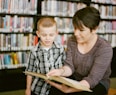 teacher reading beside boy in gray and white plaid dress shirt