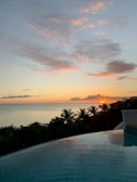 Sunset view over a serene infinity pool overlooking a tropical coastline.