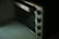 A close-up image of a stainless steel countertop oven with four control knobs is seen. The knobs are aligned vertically, and the oven door has a large handle. The surface appears clean and slightly reflective.