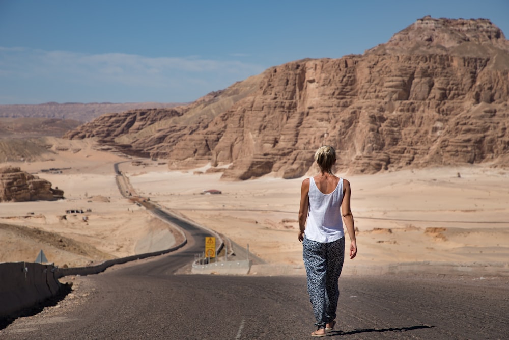 woman in white tank top and blue and white plaid pants standing on gray asphalt road