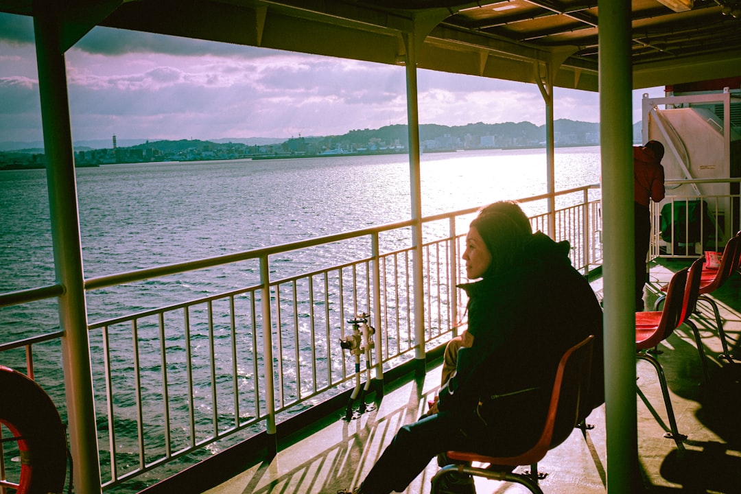 woman in black jacket sitting on chair near body of water during daytime