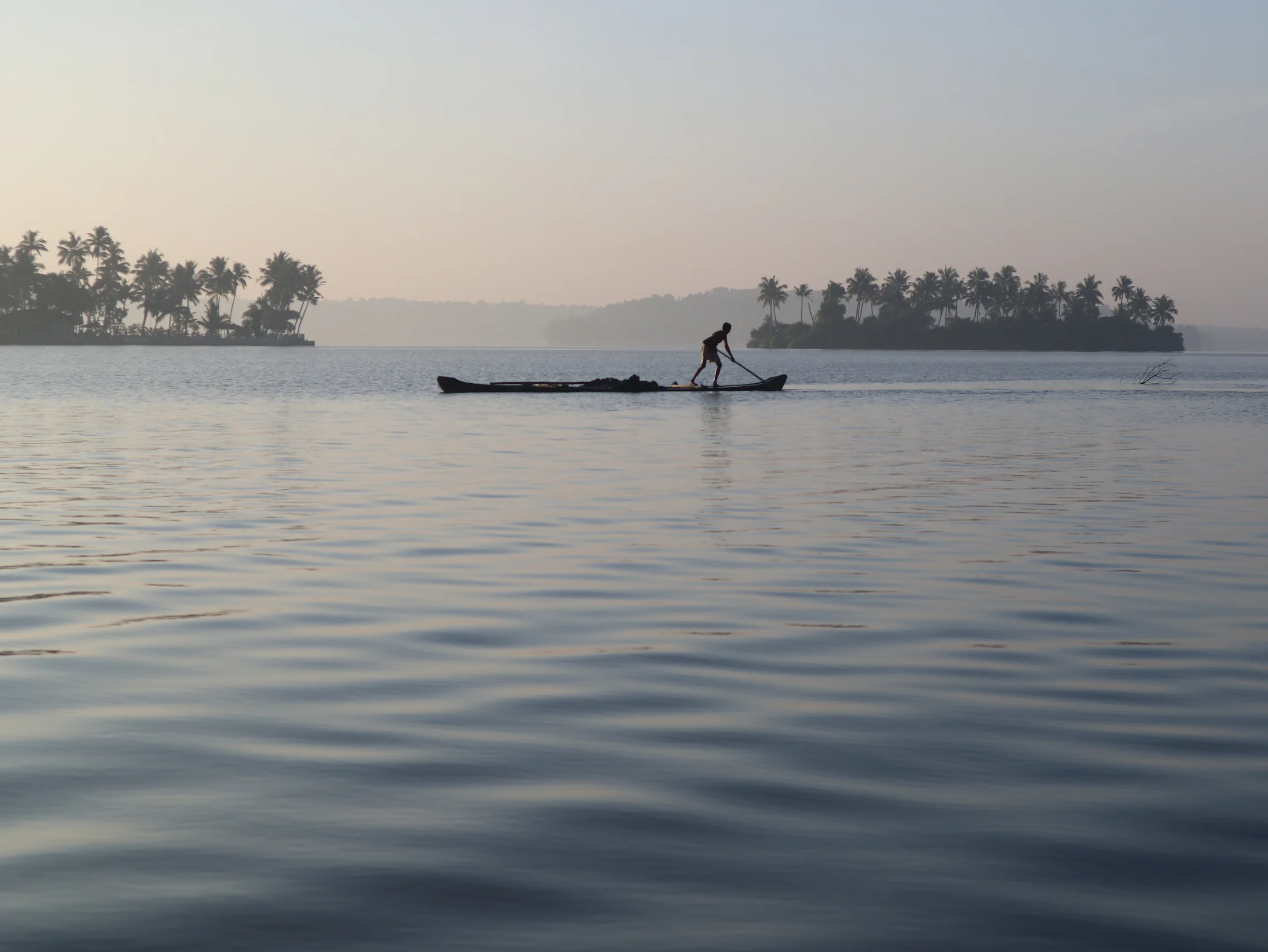 A fisherman poling a canoe across still water at sunrise on Munroe Island