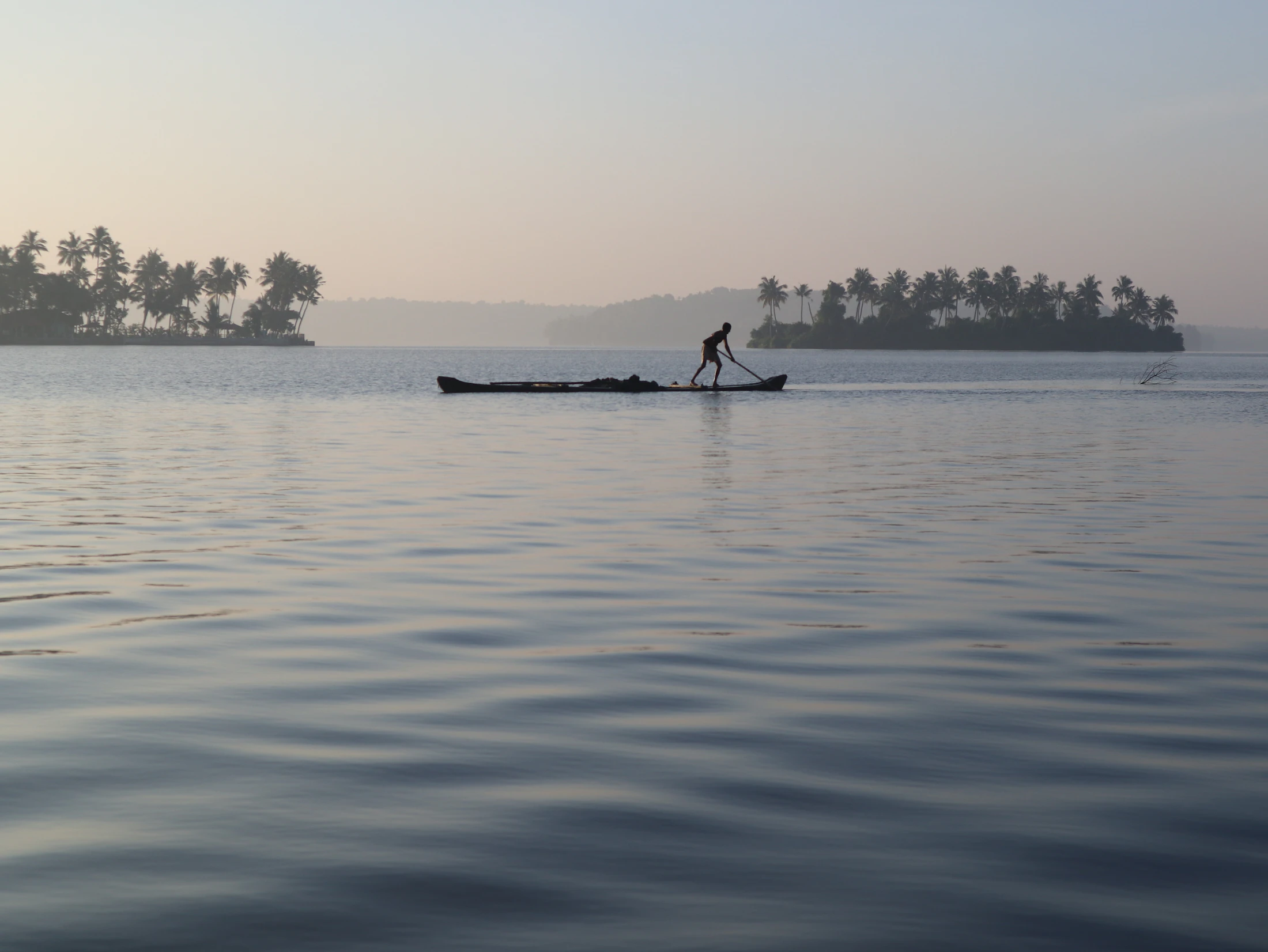 A fisherman poling a canoe across still water at sunrise on Munroe Island