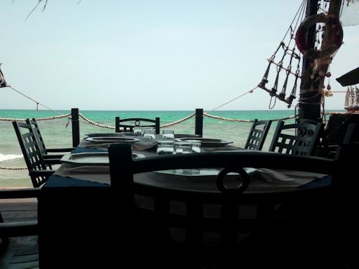 A cozy table set on the deck of a boat with plates, glasses, and a view of the sea.